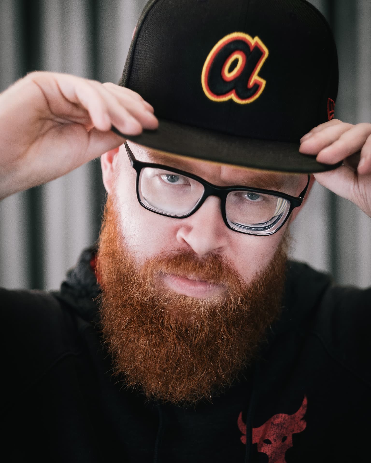 Close-up portrait of a red-bearded man tipping a baseball cap by Dan Almasy