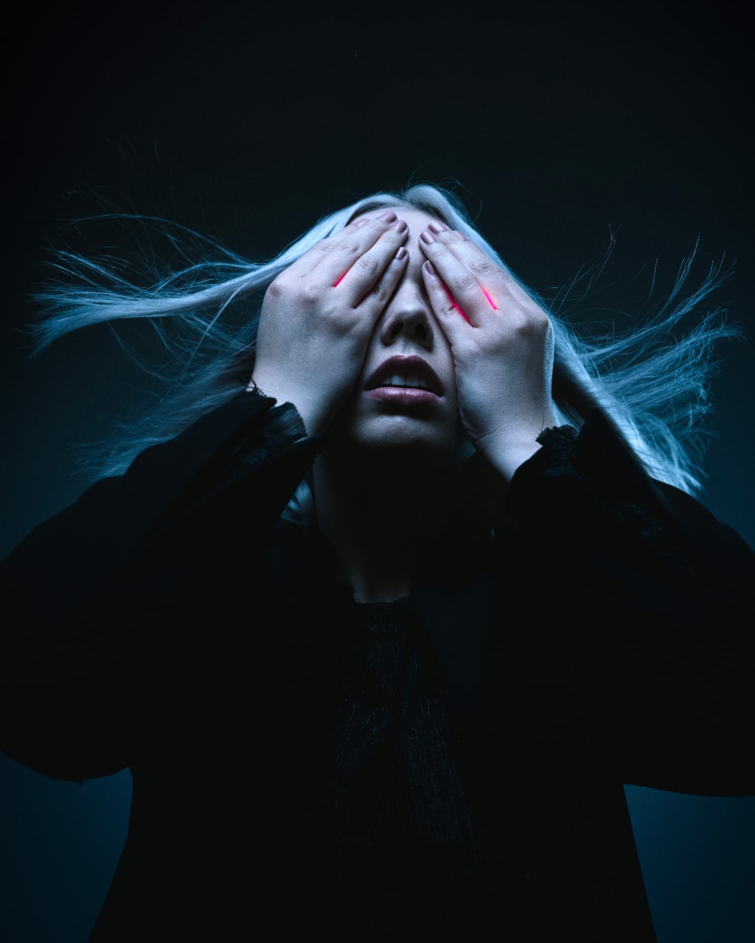 Teal-lit portrait with hands covering the eyes and windblown hair by Dan Almasy