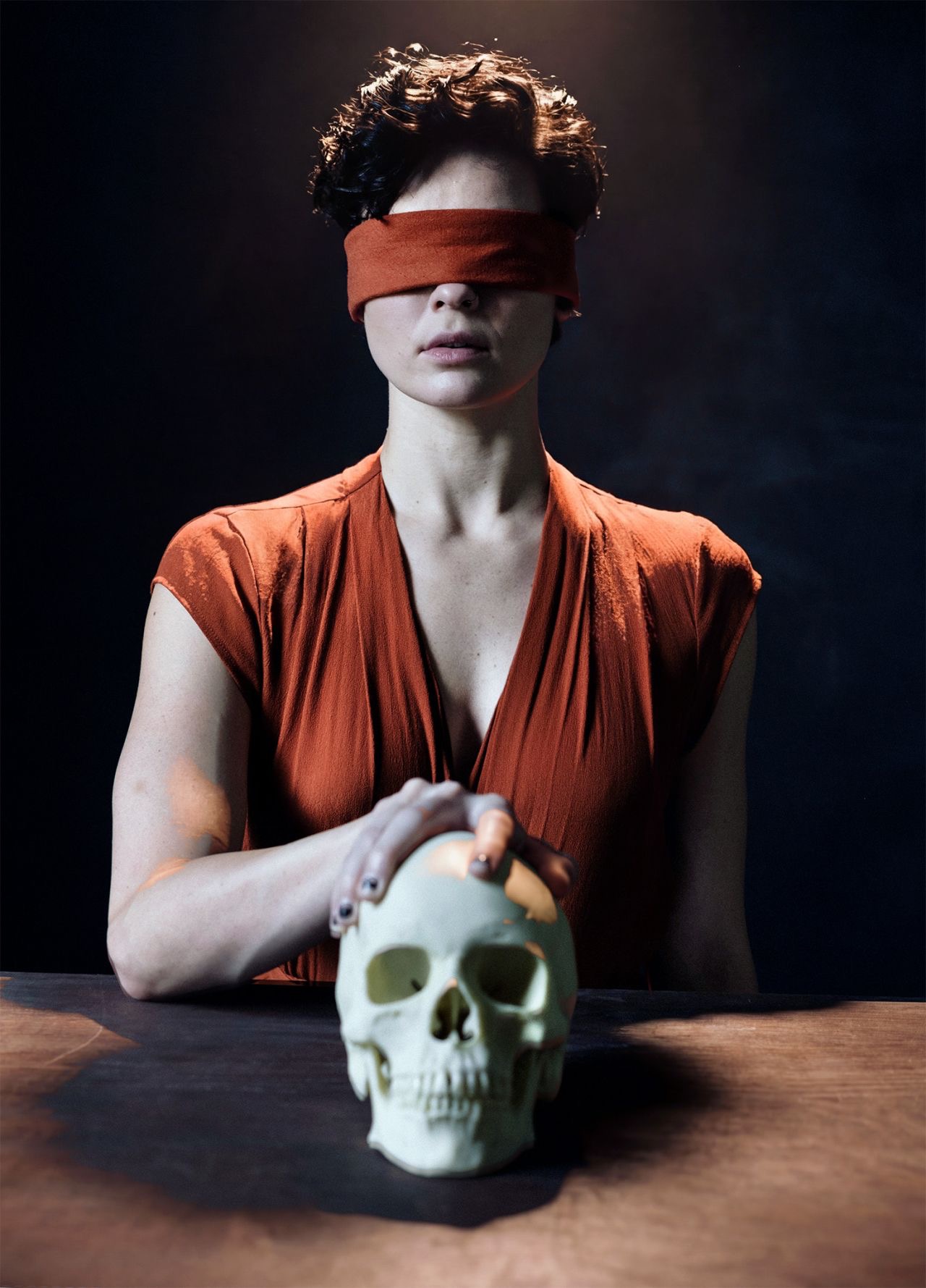 Blindfolded figure in rust silk holding a skull by Dan Almasy