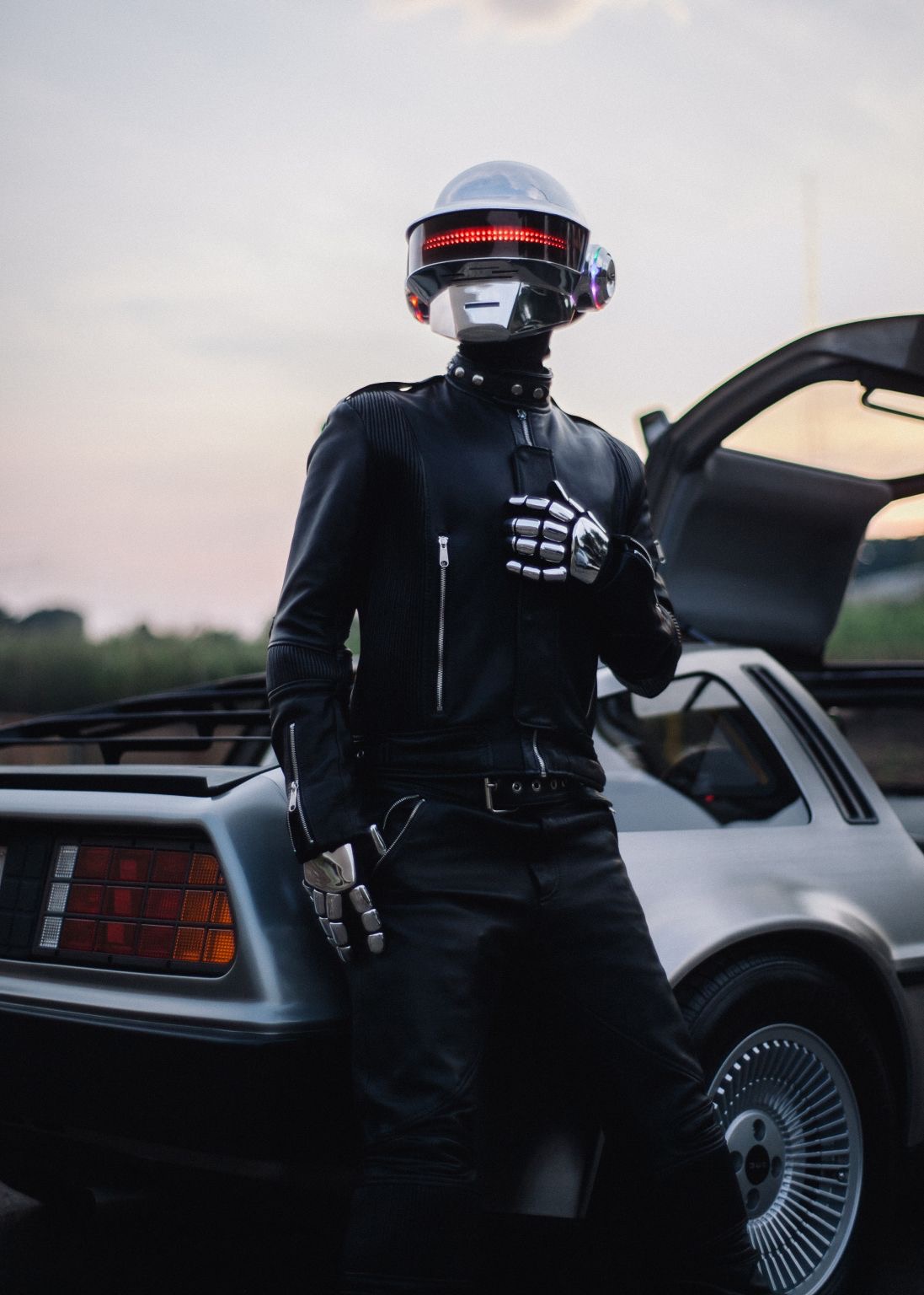 Chrome-gloved helmeted figure beside a DeLorean at sunset