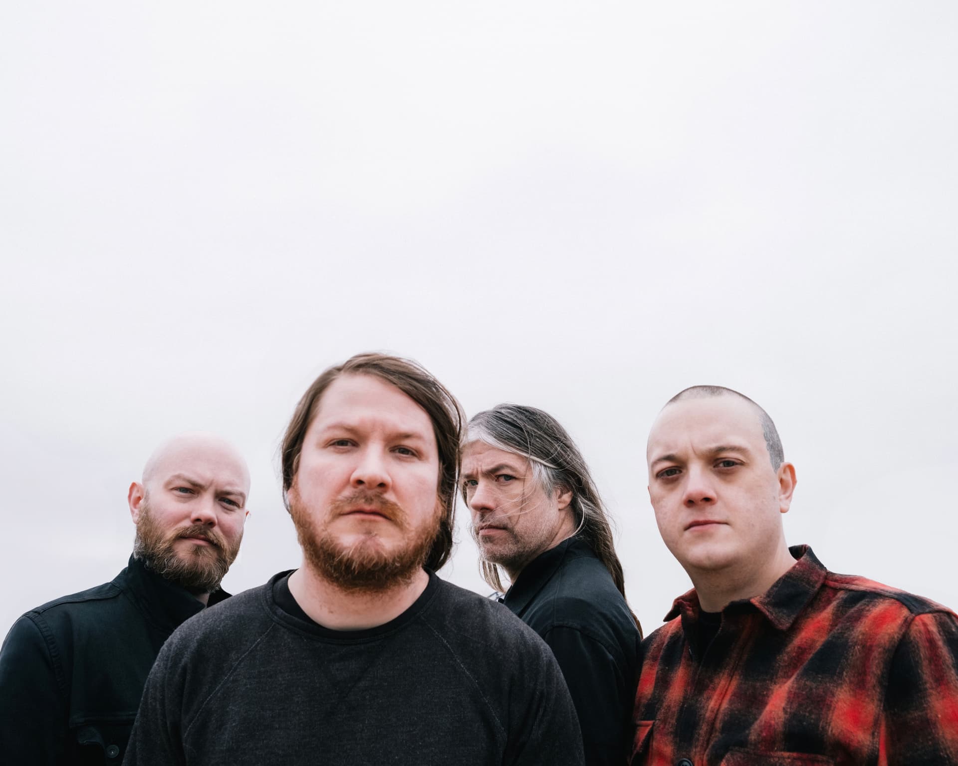 Four musicians photographed against an overcast white sky by Dan Almasy