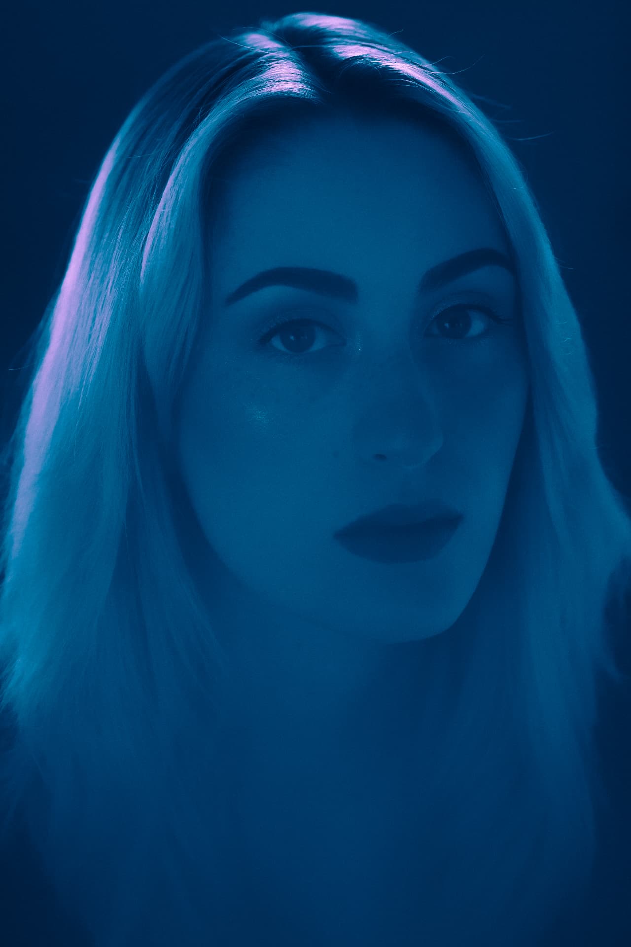 Blue-lit portrait of a blonde woman against a dark background by Dan Almasy
