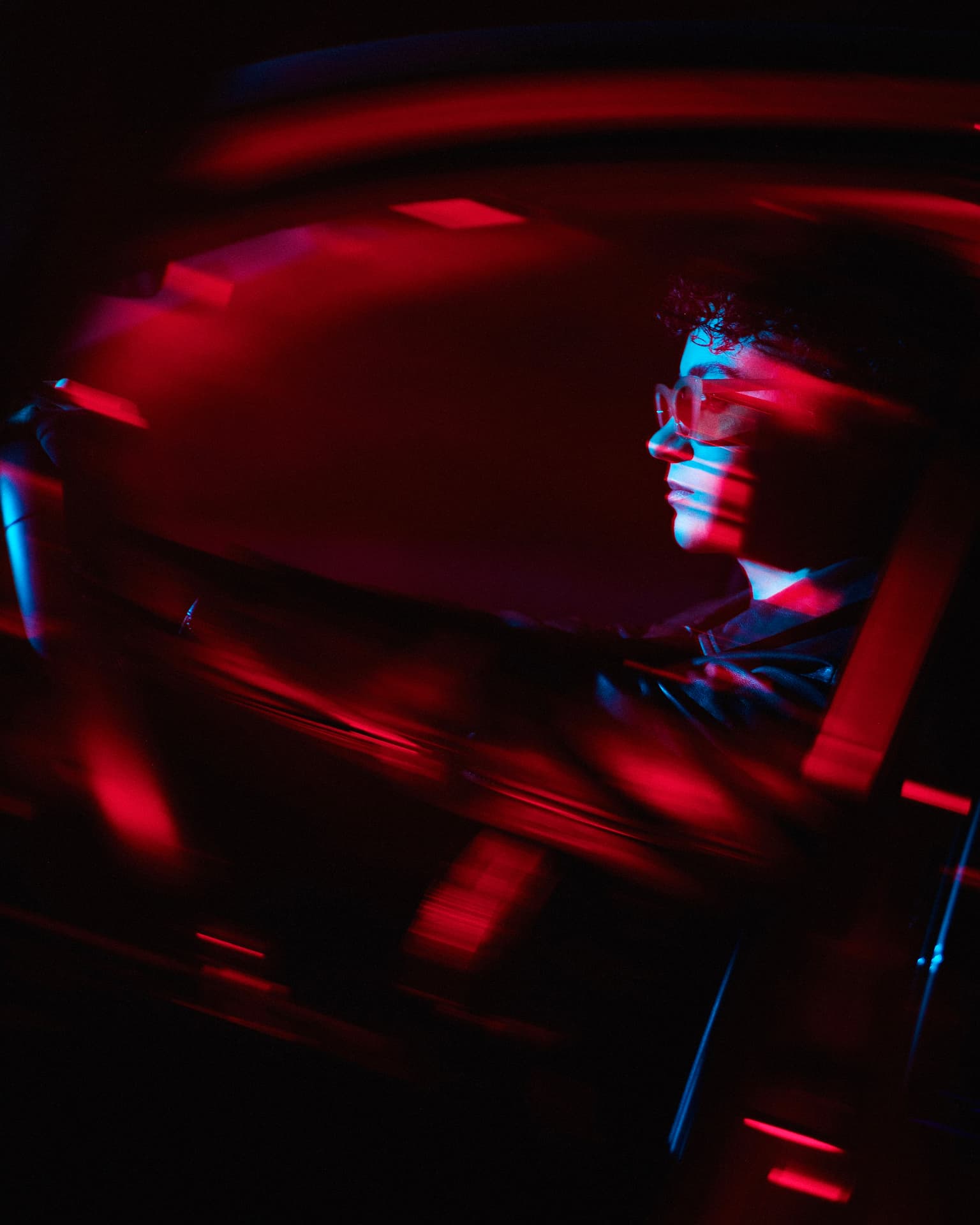 Red-lit long-exposure portrait of a driver behind the wheel by Dan Almasy