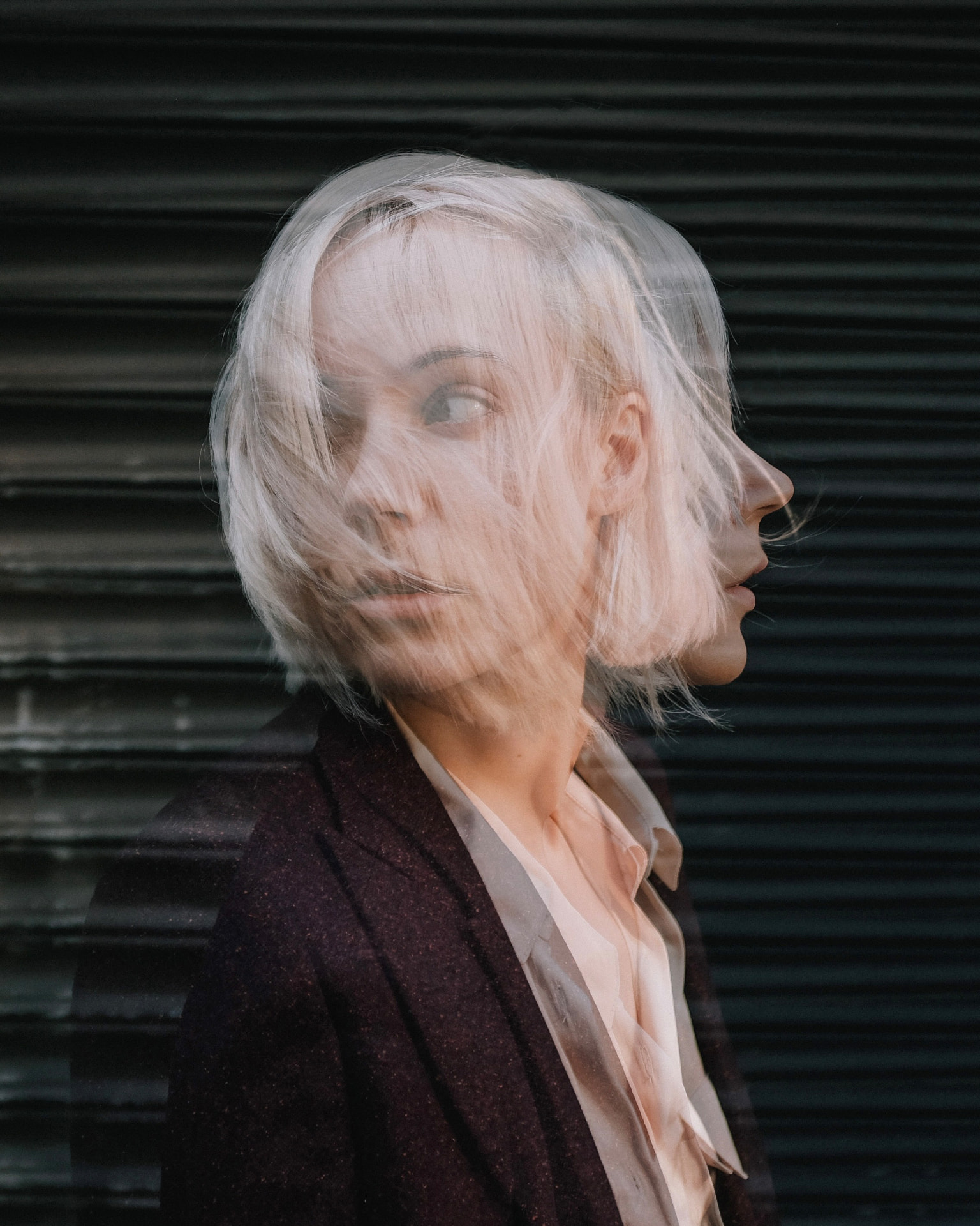 Platinum blonde portrait with motion-blurred hair against dark shutters by Dan Almasy